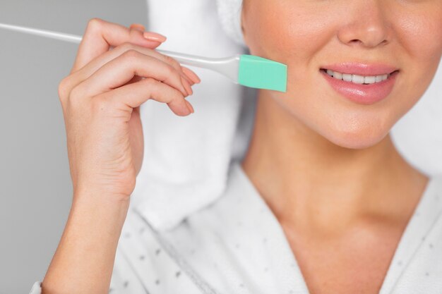 Vista frontal de la mujer sonriente en bata de baño aplicando cuidado de la piel