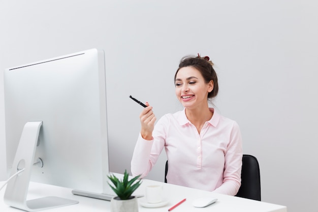 Vista frontal de la mujer sonriente en el escritorio señalando la pluma en la computadora