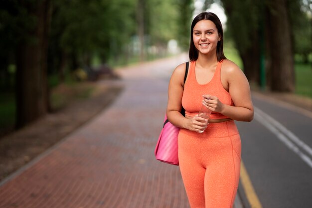 Vista frontal mujer sonriente con estera de yoga