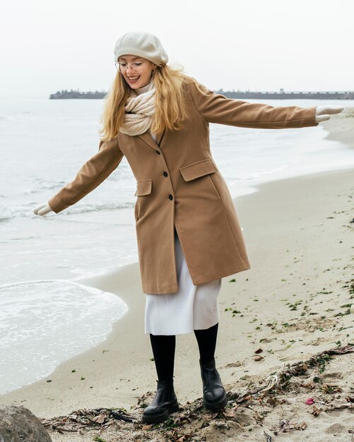 Vista frontal de la mujer sonriente con guantes en la playa durante el invierno