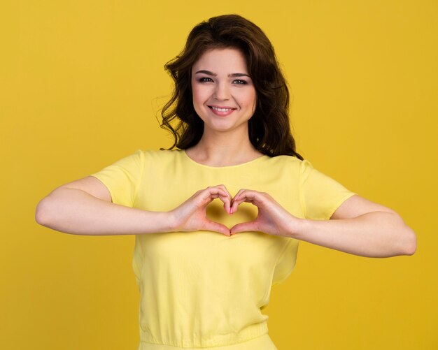 Vista frontal de la mujer sonriente haciendo signo de corazón con las manos