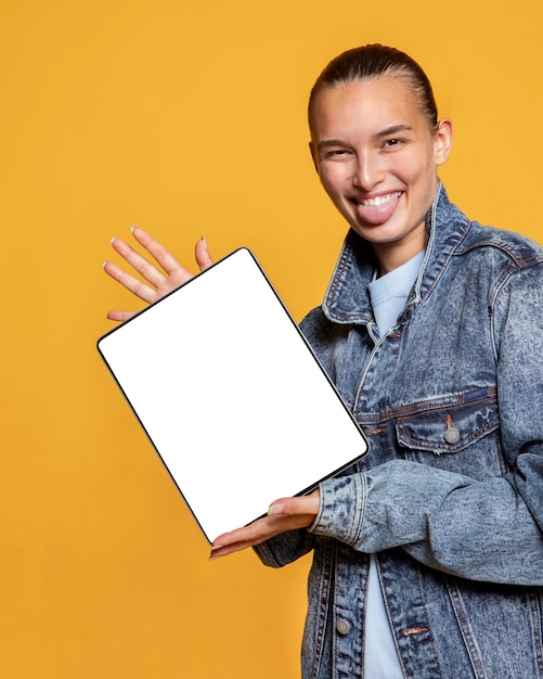 Vista frontal de la mujer sonriente con la lengua fuera sosteniendo la tableta