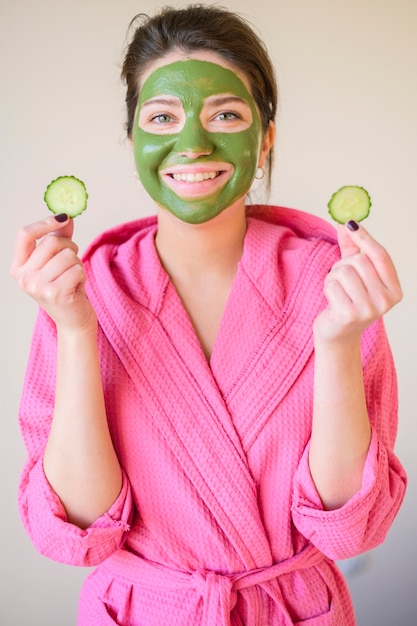 Vista frontal de la mujer sonriente con mascarilla con rodajas de pepino