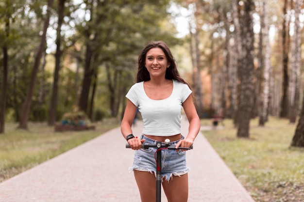 Vista frontal de la mujer sonriente montando un scooter eléctrico