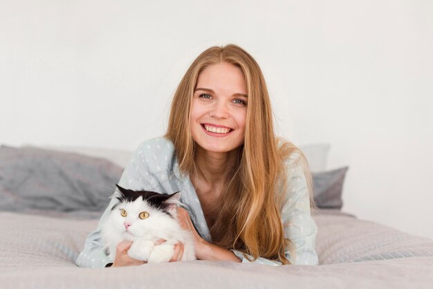 Vista frontal de la mujer sonriente en pijama en casa en la cama con gato