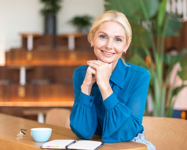 Vista frontal de la mujer sonriente posando mientras toma un café y trabaja