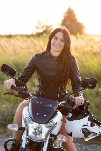 Vista frontal de la mujer sonriente posando en su motocicleta