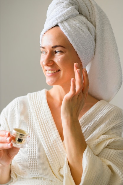 Vista frontal de la mujer sonriente que aplica la crema en la cara en casa