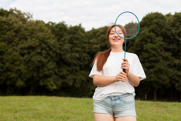 Vista frontal de la mujer sonriente con raqueta al aire libre