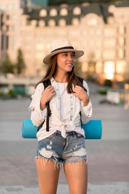 Vista frontal de la mujer sonriente con sombrero con mochila mientras viaja solo