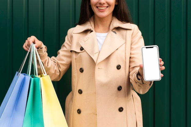 Vista frontal de la mujer sonriente sosteniendo un teléfono inteligente y bolsas de la compra.