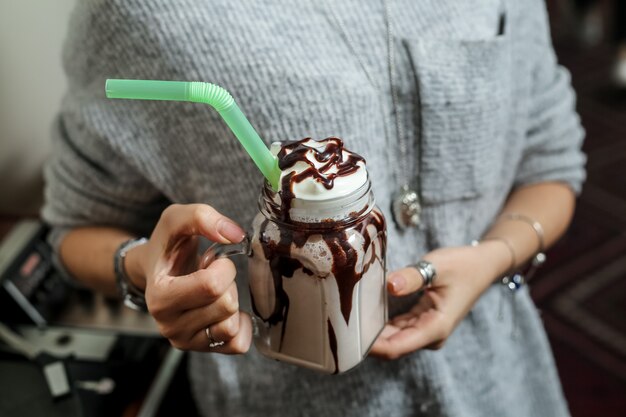 Vista frontal mujer sosteniendo batido de chocolate con glaseado de chocolate y paja verde