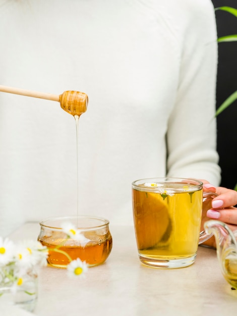 Vista frontal mujer sosteniendo cucharón de miel y vaso con té