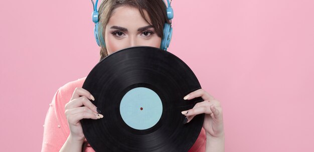 Vista frontal de la mujer sosteniendo un disco de vinilo mientras usa auriculares