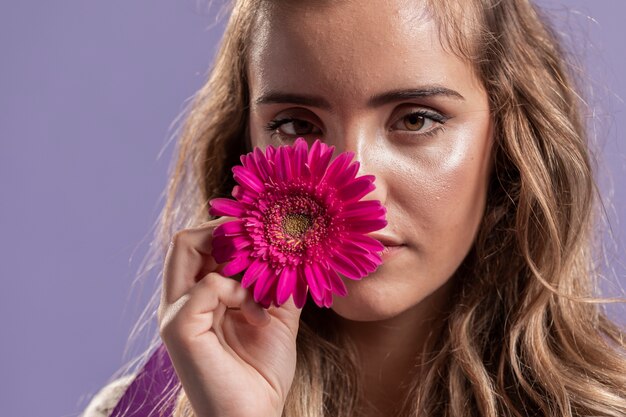 Vista frontal de la mujer sosteniendo una flor cerca de su cara