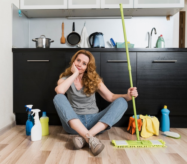 Vista frontal de la mujer sosteniendo la fregona con productos de limpieza