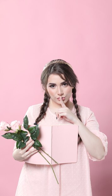 Vista frontal de la mujer sosteniendo el libro y las rosas y poniendo el dedo sobre la boca