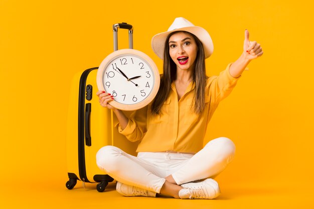 Vista frontal de la mujer sosteniendo el reloj y dando pulgares arriba