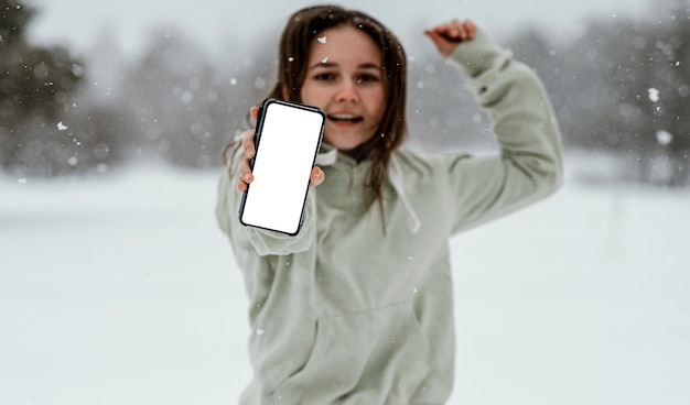 Vista frontal de la mujer sosteniendo el teléfono inteligente y saltando en el aire al aire libre en invierno