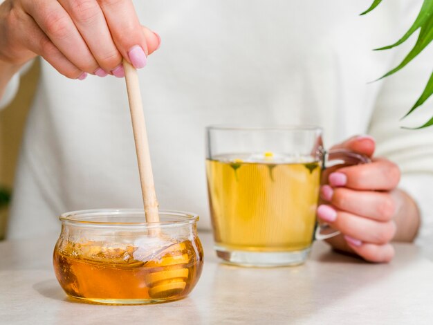 Vista frontal mujer sosteniendo el vaso con té y cazo en tarro de miel