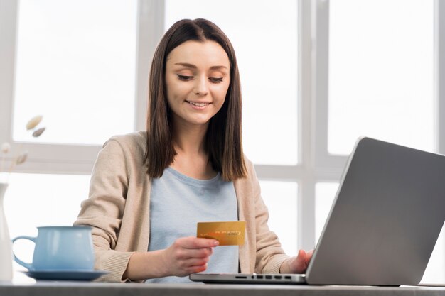 Vista frontal de la mujer con tarjeta de crédito y trabajando en la computadora portátil