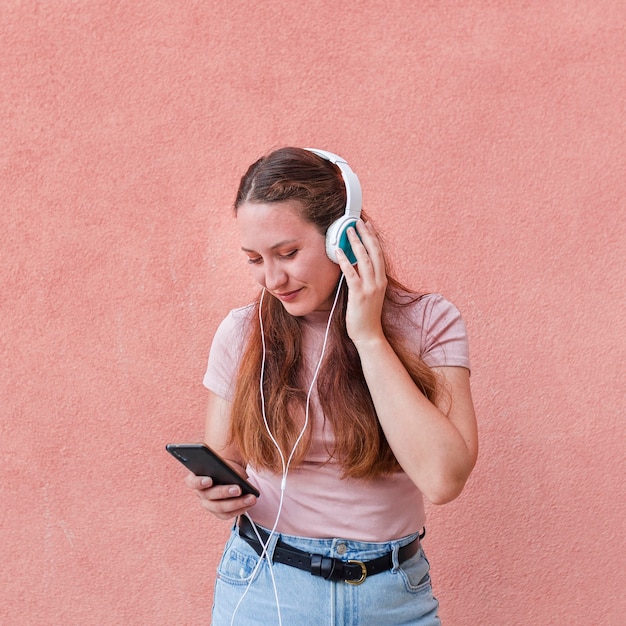 Vista frontal de la mujer con teléfono inteligente y auriculares para escuchar música