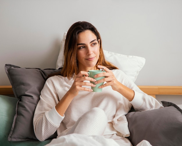 Vista frontal de la mujer tomando un café en la cama