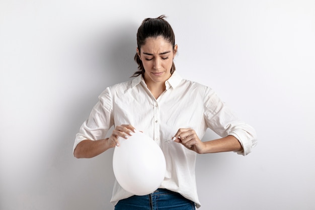 Vista frontal de la mujer tratando de hacer estallar un globo