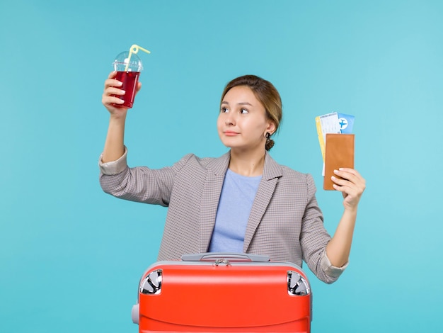 Vista frontal mujer en vacaciones con jugo de cereza fresco y boletos en el fondo azul viaje en avión viajes de vacaciones