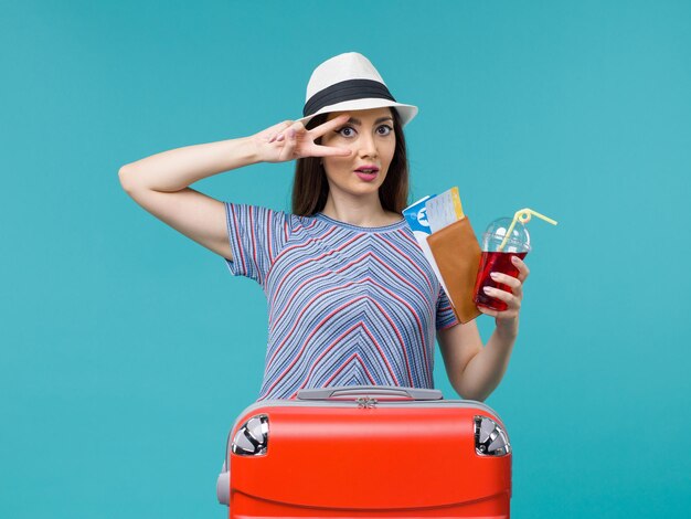 Vista frontal de la mujer en vacaciones sosteniendo jugo con boletos en el escritorio azul viaje viaje mar femenino avión de verano