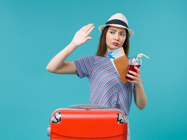 Vista frontal mujer en vacaciones sosteniendo jugo con boletos en el fondo azul viaje mar femenino viaje en avión de verano