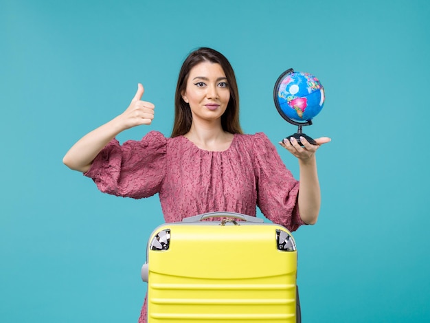 Vista frontal mujer en vacaciones sosteniendo un pequeño globo terráqueo sobre el fondo azul mar vacaciones viaje viaje verano mujer