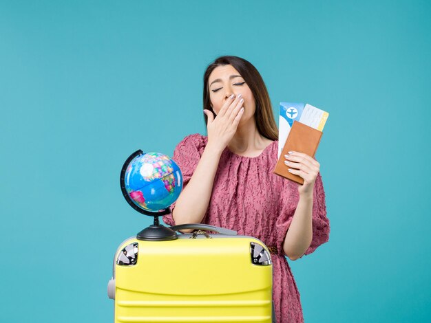 Vista frontal mujer en vacaciones sosteniendo su billetera y boleto bostezando sobre fondo azul viaje al mar vacaciones mujer viaje viaje