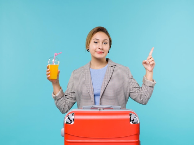 Vista frontal mujer de vacaciones con su bolsa roja con jugo fresco en el escritorio azul viaje en avión de vacaciones viaje por mar