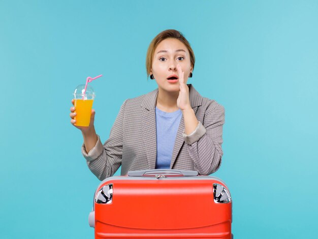 Vista frontal mujer de vacaciones con su bolsa roja con jugo fresco sobre el fondo azul mar vacaciones avión viaje viaje viaje