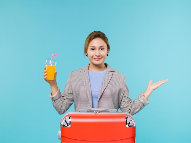 Vista frontal mujer de vacaciones con su bolsa roja con jugo fresco sobre el fondo azul viaje en avión de vacaciones viaje por mar