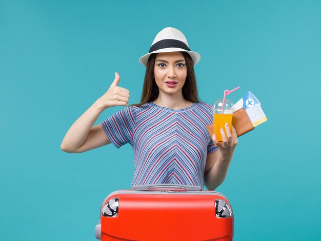 Vista frontal de la mujer de vacaciones con su bolsa roja sosteniendo boletos y jugo sobre un fondo azul viaje viaje viaje vacaciones hembra