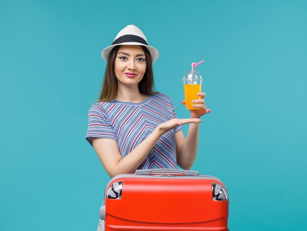 Vista frontal de la mujer de vacaciones con su bolsa roja sosteniendo su jugo en el fondo azul viaje viaje vacaciones viaje femenino