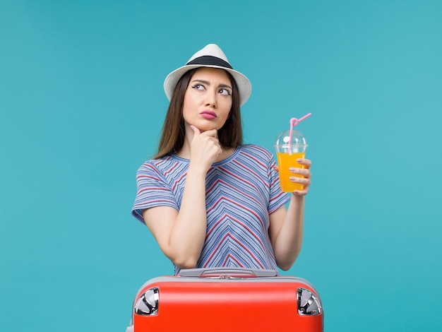 Vista frontal de la mujer de vacaciones con su bolsa roja sosteniendo su jugo en el fondo azul viaje viaje viaje vacaciones hembra