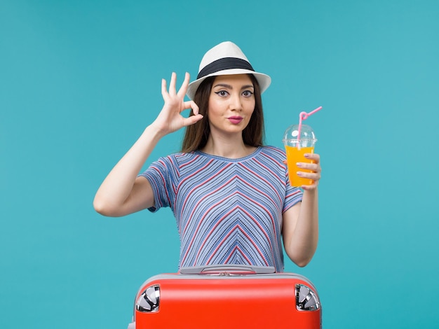 Vista frontal de la mujer de vacaciones con su bolsa roja sosteniendo su jugo en el fondo azul viaje viaje viaje vacaciones hembra