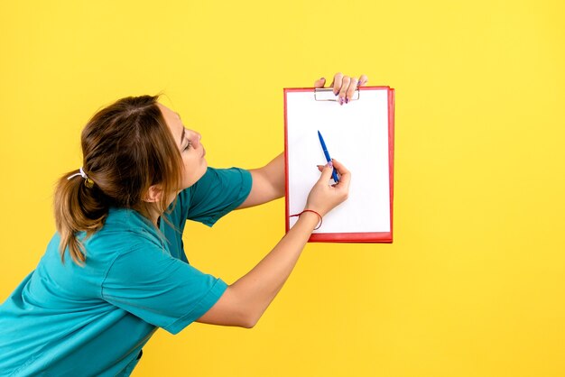 Vista frontal de la mujer veterinaria sosteniendo análisis sobre pared amarilla