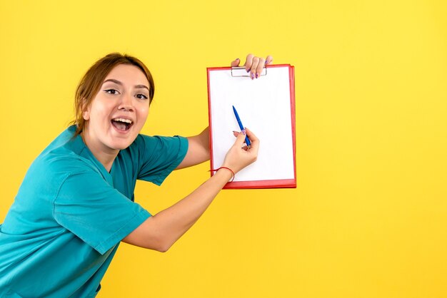 Vista frontal de la mujer veterinaria sosteniendo análisis sobre pared amarilla