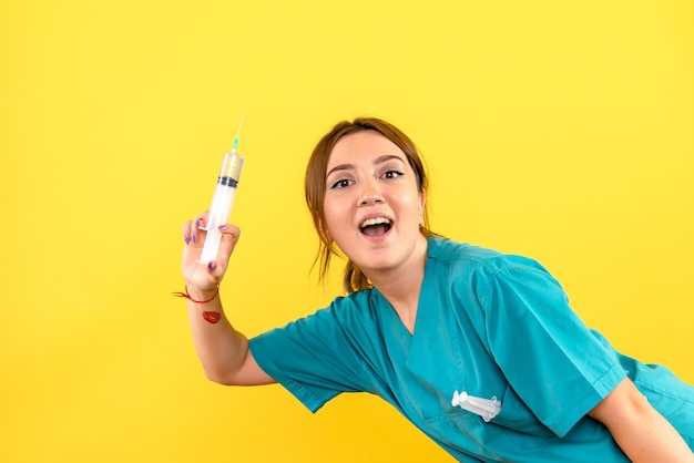 Vista frontal de la mujer veterinaria sosteniendo una inyección enorme en la pared amarilla