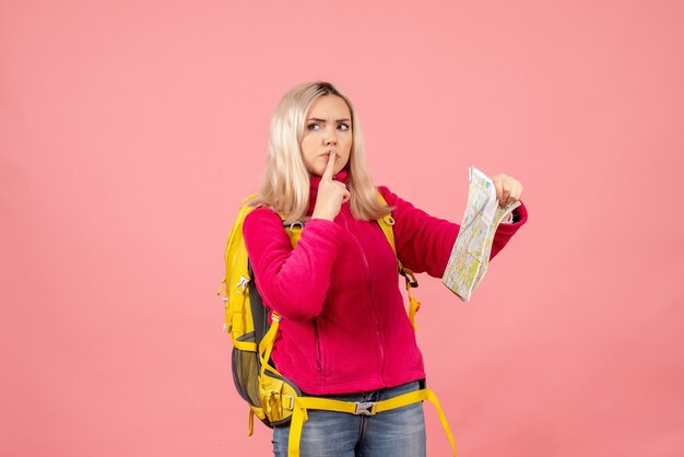 Vista frontal mujer viajera confundida con mochila amarilla con mapa haciendo señal de silencio