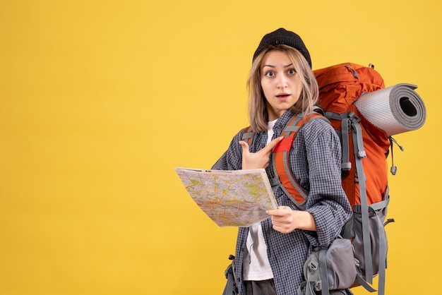 Vista frontal de la mujer viajera confundida con mochila sosteniendo el mapa apuntando a sí misma