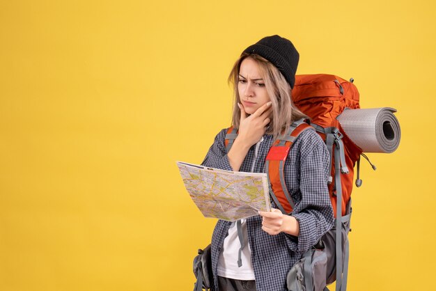 Vista frontal de la mujer viajera ocupada con mochila mirando el mapa pensando en su viaje