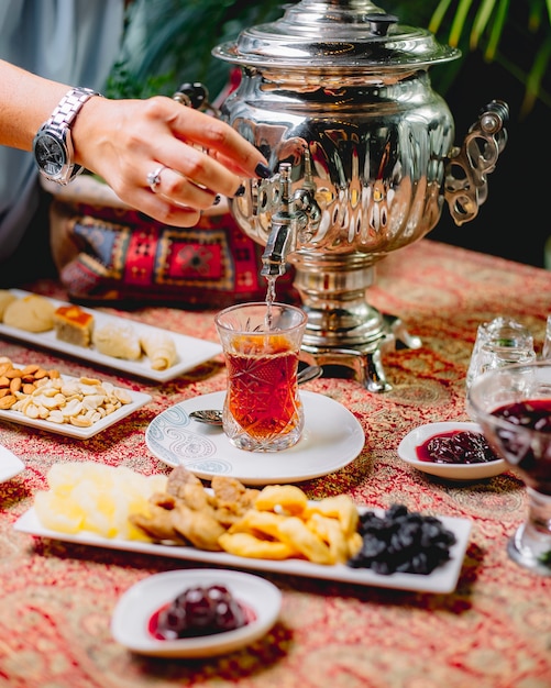 Foto gratuita vista frontal, una mujer vierte té de una tetera de samovar en un vaso de armuda en un plato