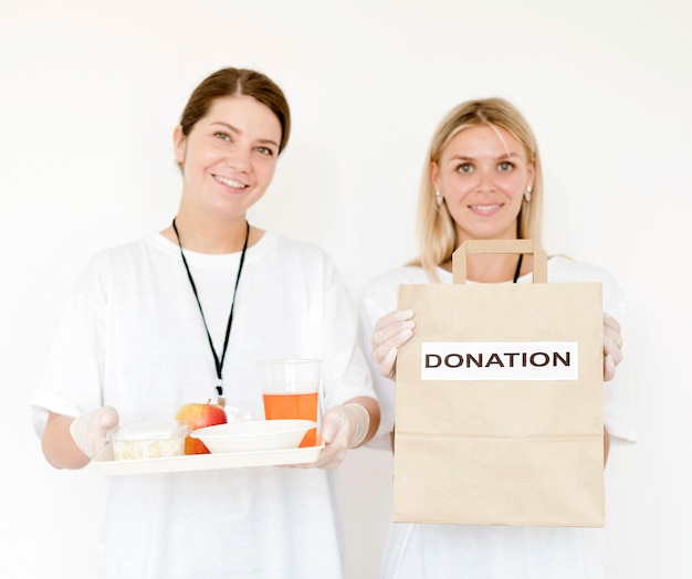 Vista frontal de mujeres con bolsa de donación y comida
