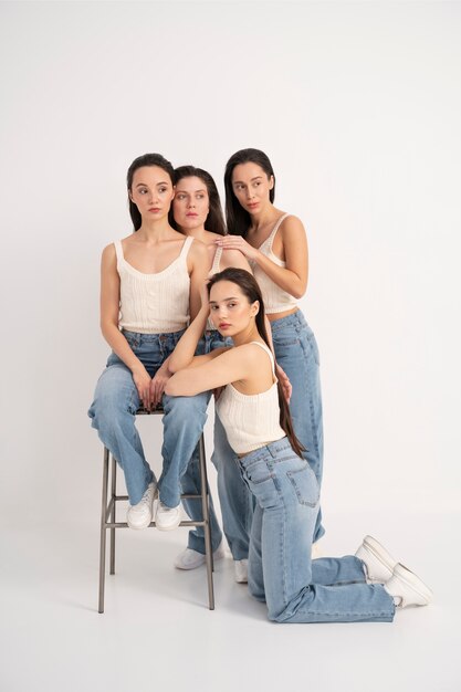 Vista frontal de mujeres en camisetas sin mangas y jeans posando con silla en retratos minimalistas