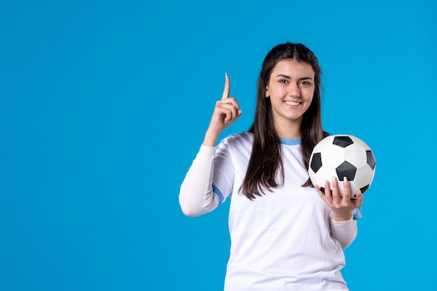 Vista frontal de las mujeres jóvenes con balón de fútbol en la pared azul